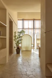 A bright and welcoming hallway with a large window, two potted plants, and a vase, filled with natural light