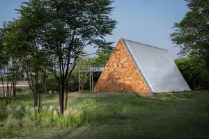 A unique wooden building with a triangular shape, blending modern architecture with natural surroundings
