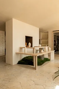 A minimalist interior design showroom featuring a table with six vases of various sizes and shapes, set against a clean white wall