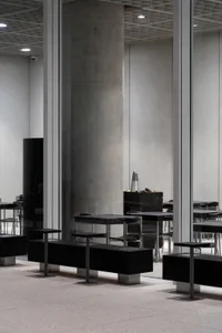 Empty restaurant interior with concrete walls and floors, dimly lit with tables and chairs arranged throughout the space