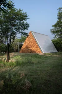 A modern house with a triangular shape, wooden exterior, and large window, illuminated by sunlight with shadows cast on the structure