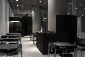 A bustling restaurant interior with brick and concrete walls, multiple dining tables, and chairs, featuring a mix of natural and artificial lighting