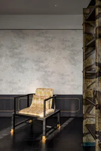 A cozy living space with a chair in front of a wall featuring a patterned wallpaper, with a wooden chair and yellow and black striped upholstery