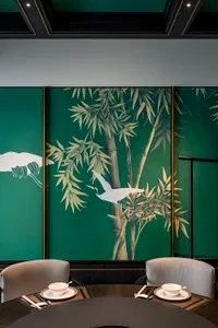 Serene living space with green walls, artwork of birds on bamboo trees, and two chairs in a calming environment