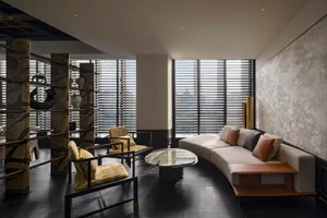 Modern living room with hardwood floors, black walls, and large windows allowing natural light to enter, featuring two couches, three chairs, and a dining table