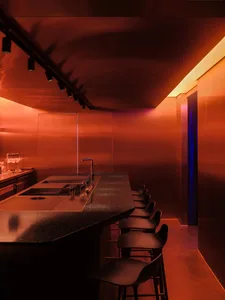 A cozy bar area with a long counter and stools, featuring bottles and an inviting atmosphere
