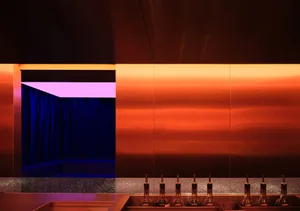 A kitchen and dining area with two sinks, a marble countertop, and a dining table, set against a backdrop of warm orange and blue tones