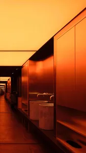 A hotel corridor with orange walls, two sinks, mirrors, and trash cans, suggesting a clean and well-maintained environment