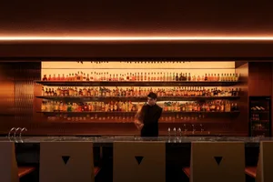 A man stands in front of a bar with numerous bottles of liquor and wine glasses, suggesting a social gathering or event