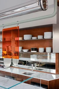 A modern kitchen with a dining table, sink, and plates on display, featuring marble countertops and a clean, well-lit atmosphere