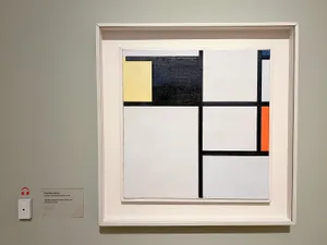 Black and white abstract art piece featuring a square grid pattern with various shapes and colors within each square, displayed on a wall