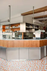 A casual dining bar with a wooden counter, bottles, cups, bowls, and wine glasses, set in a warm and inviting atmosphere