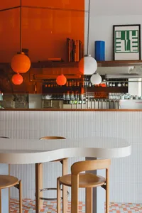 A cozy restaurant dining area with a white table surrounded by chairs, bottles, and warm wood elements