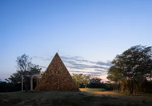 A unique triangular building with a blend of traditional and modern architectural elements, possibly made of wood, with a mix of textures and natural light