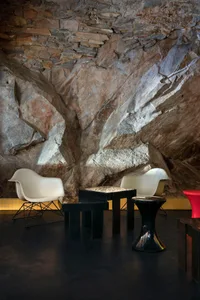 Cozy modern living space with a large rock wall, two white chairs, and a dining table, dimly lit for an intimate ambiance