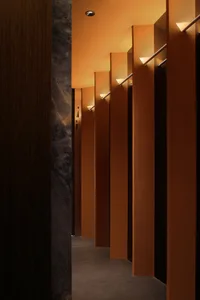A functional hallway with concrete walls, lined with three identical doors and light fixtures above each door