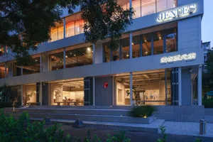 A modern building with white walls, glass windows, and potted plants, featuring a spacious and contemporary design with scattered chairs