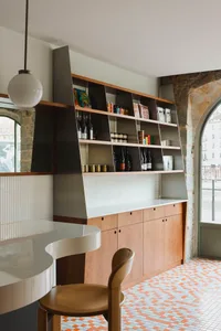 A cozy kitchen with a countertop island, sink, and wine rack, surrounded by bottles and books, with a focus on functionality and organization