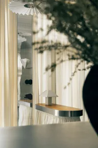 A wooden table with a silver base and lamp, surrounded by curtains in a cozy room for relaxation or dining