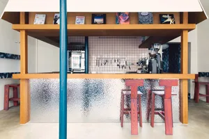 Cozy modern kitchen with wooden floors, walls, and a counter with stools and a coffee maker, surrounded by scattered books