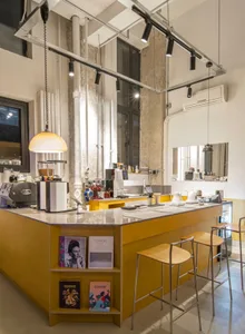 Modern kitchen with wooden floors, white walls, and a yellow countertop, featuring stools, a refrigerator, and various items on the counter