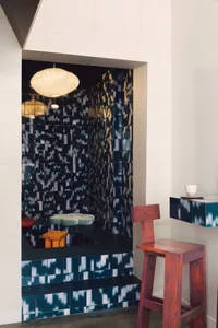 A modern dining space with black and white checkered walls, a red chair, an orange chair, and a dining table, creating an inviting and comfortable atmosphere
