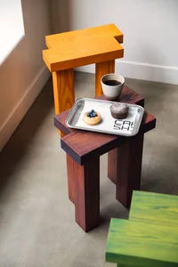 A cozy coffee shop interior with a wooden chair, hardwood floor, and a window, featuring a tray with donuts and coffee
