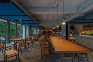 An open-concept restaurant interior with a large wooden dining table and numerous chairs, featuring a modern design with sleek lines and minimalistic decorations, and soft diffused lighting