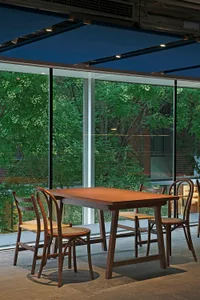 A modern dining space with a wooden table and chairs, surrounded by large windows that provide natural light