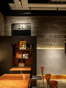 Modern interior design showroom with a wooden table and chair set up in front of a brick wall, featuring books and a minimalist atmosphere