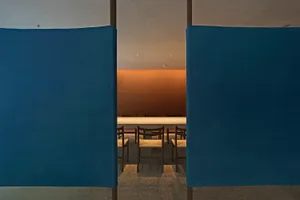 A calm and inviting dining space with a long table and chairs, surrounded by brown walls and well-lit by natural or artificial light