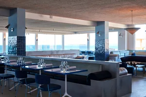 A modern restaurant interior with a large dining area featuring wooden tables and chairs, wine glasses, and an inviting atmosphere