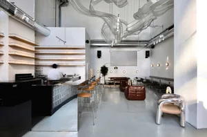 Modern restaurant interior with a bar area, dining tables, potted plants, and comfortable seating