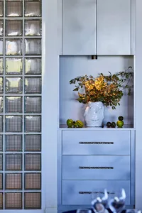 A modern kitchen with a white cabinet, glass door, and potted plants with green leaves and a vase with yellow flowers, creating a bright and inviting atmosphere