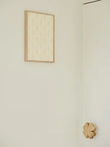A clean and minimalistic room with a white wall featuring two framed pictures, one with a yellow background and the other with a brown frame, and two wooden decorative elements at the bottom