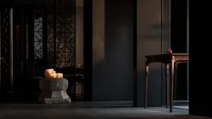 A dimly lit dining room with a modern aesthetic, featuring a wooden table and stone elements, surrounded by chairs and candles