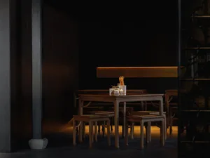 A dark and intimate restaurant with wooden tables and chairs arranged in rows, creating a warm and inviting atmosphere
