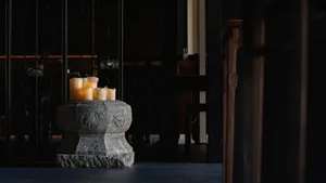 A calm and inviting dining space with a black and white color scheme, featuring a stone pedestal with lit candles, two chairs, and a dining table