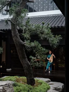 An Asian woman plays a musical instrument on a wooden stage with two chairs nearby, set in an oriental cultural event or celebration