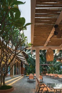 Outdoor dining area with a thatched roof, palm trees, and comfortable seating with cushions