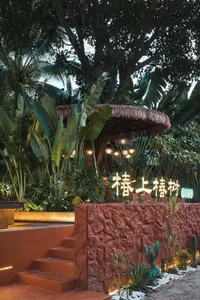 A serene outdoor patio area with a red brick wall, staircase, and small hut-like structure surrounded by palm trees and potted plants