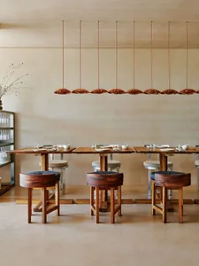 Warm and inviting restaurant interior with a long wooden dining table, chairs, cups, bowls, vases, and wine glasses