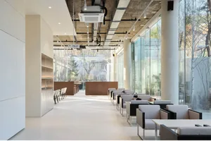 Bright and inviting restaurant interior with a large dining area featuring wood and glass elements, natural light, and a mix of chairs and booth-style seating