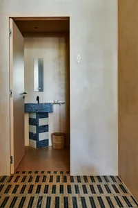 A well-lit bathroom with a sink on the left, a mirror above it, and a toilet in the corner, surrounded by white walls