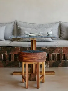 Modern living room with grey couches, a wooden chair, and a marble countertop, featuring a dining table with cups, bowls, and a vase, in an elegant and sophisticated atmosphere