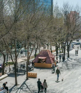 繁忙的城市街景，建築前有一座小型木構建築，包含行人、車輛與紅綠燈