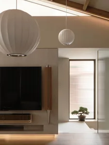 Cozy living space with a flat screen TV above a fireplace, white lamps, and a potted plant adding a touch of greenery