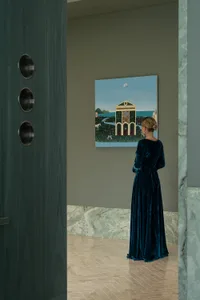 A woman admires a painting of a building with a large dome, set against a neutral background