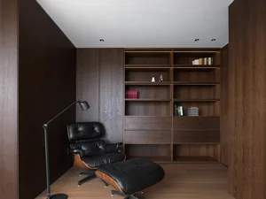 Cozy living room with a black leather chair, wooden floors and walls, and a bookshelf, lit by a lamp
