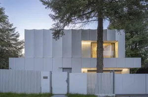 A modern house with a concrete exterior, large windows, and a tree in front